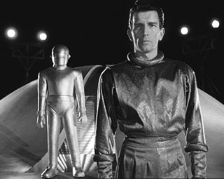 In The Day the Earth Stood Still (1951), Michael Rennie (right) as Klaatu with giant robot Gort (background), aliens with a warning for Earth.
